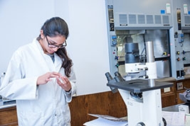 a student with dark hair in a lab coat standing next to a microscope